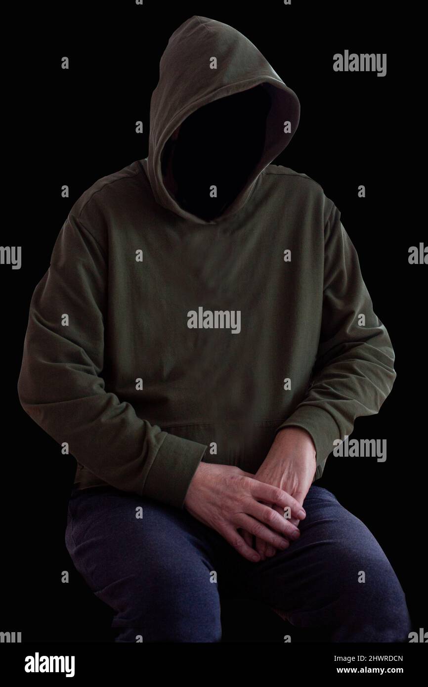 Personne sans visage dans le sweat à capuche assis dans l'obscurité avec les mains croisées. Homme mystère avec capot. Hoodie de hooligan. Crime et violence Banque D'Images