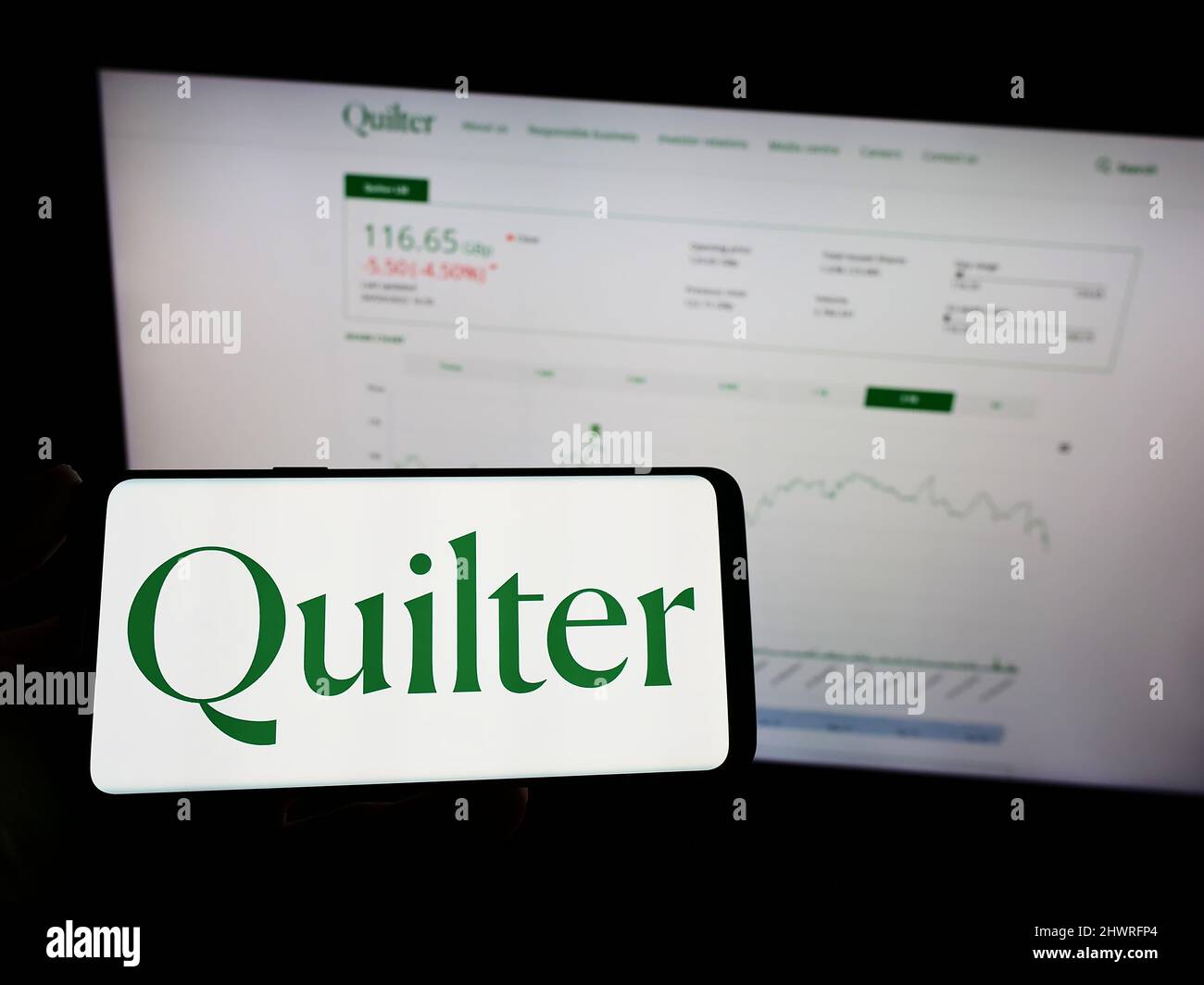 Personne tenant un téléphone portable avec le logo de la société britannique de gestion de patrimoine Quilter plc à l'écran en face de la page Web. Mise au point sur l'affichage du téléphone. Banque D'Images