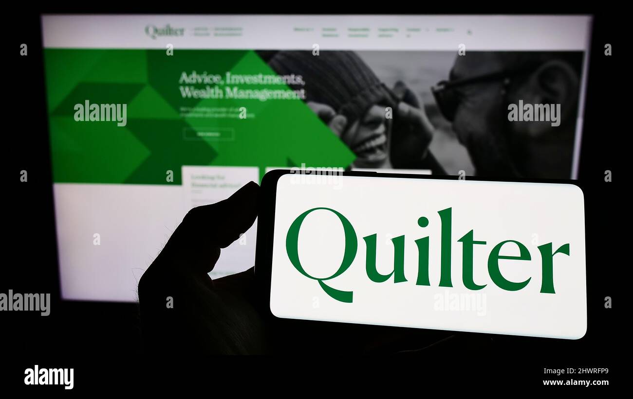 Personne tenant un téléphone portable avec le logo de la société britannique de gestion de patrimoine Quilter plc à l'écran en face de la page Web d'affaires. Mise au point sur l'affichage du téléphone. Banque D'Images