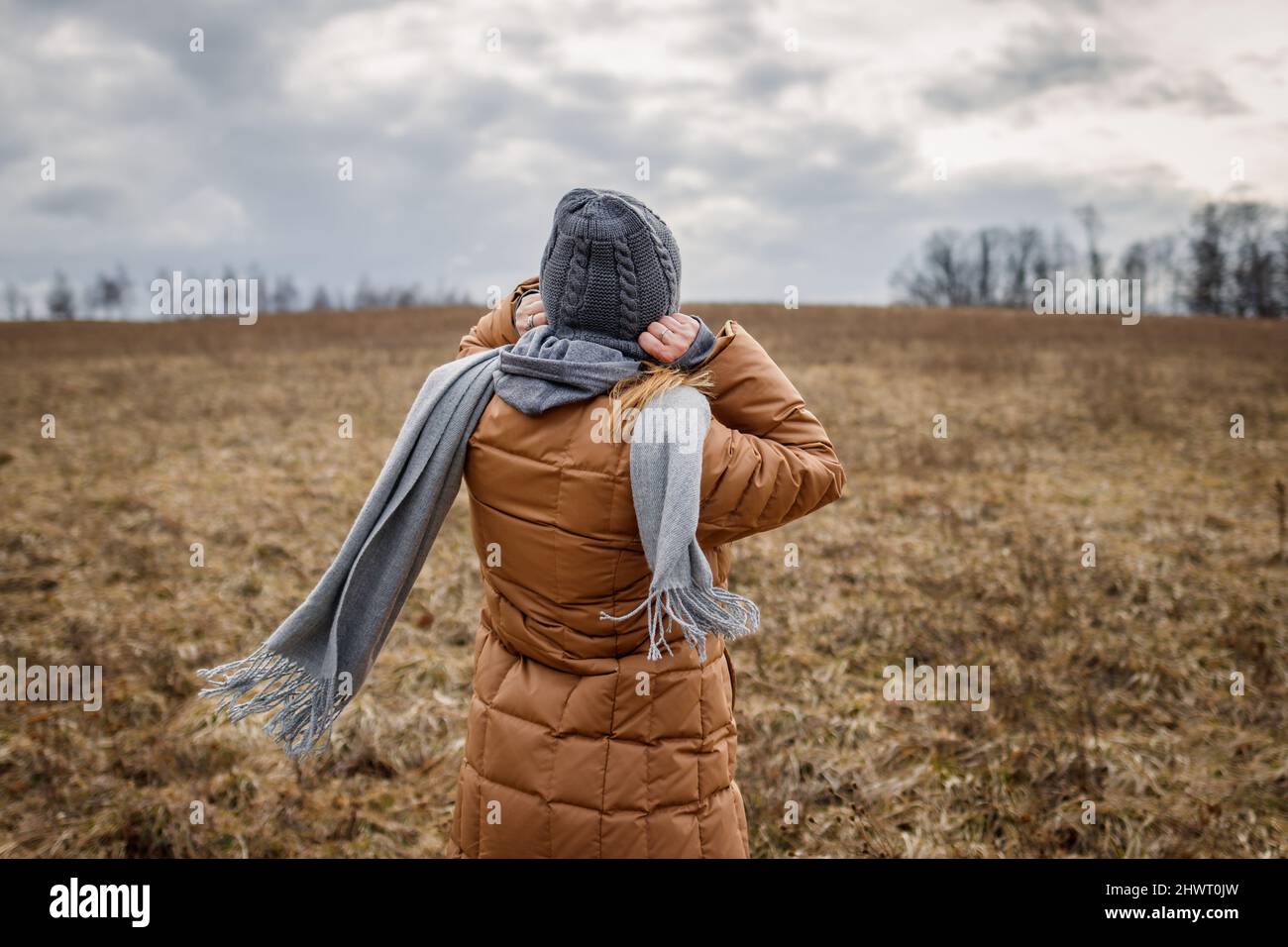 Vent et temps froid. Femme portant un manteau, une écharpe et un chapeau en tricot à l'extérieur. La femme marche dans la nature Banque D'Images