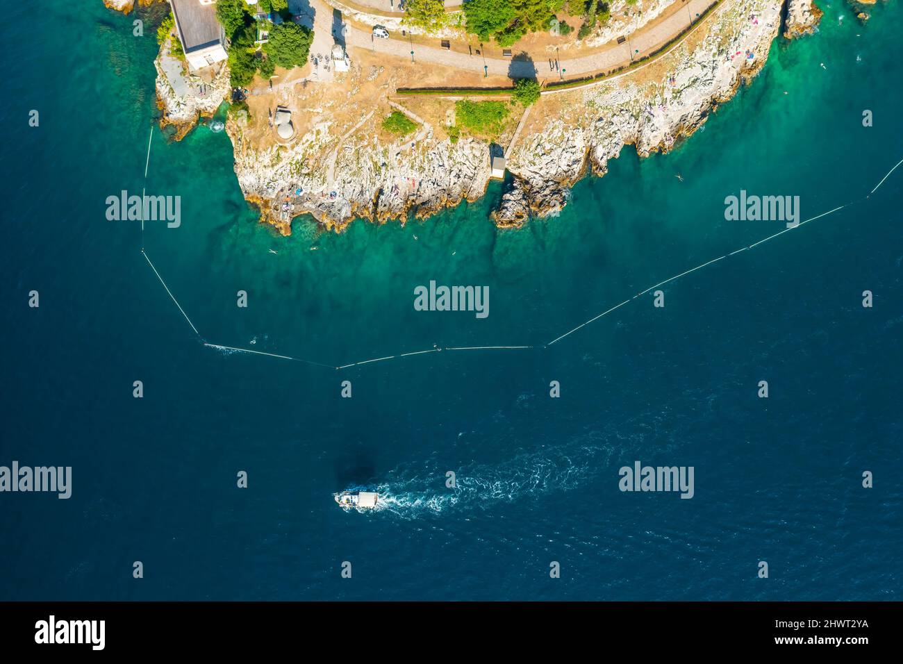 Le yacht navigue dans la mer Adriatique et laisse le sentier blanc de la mer près de la plage rovinj rocheuse. Baie d'azur entourant la ville croate à la lumière du soleil. Vue aérienne Banque D'Images