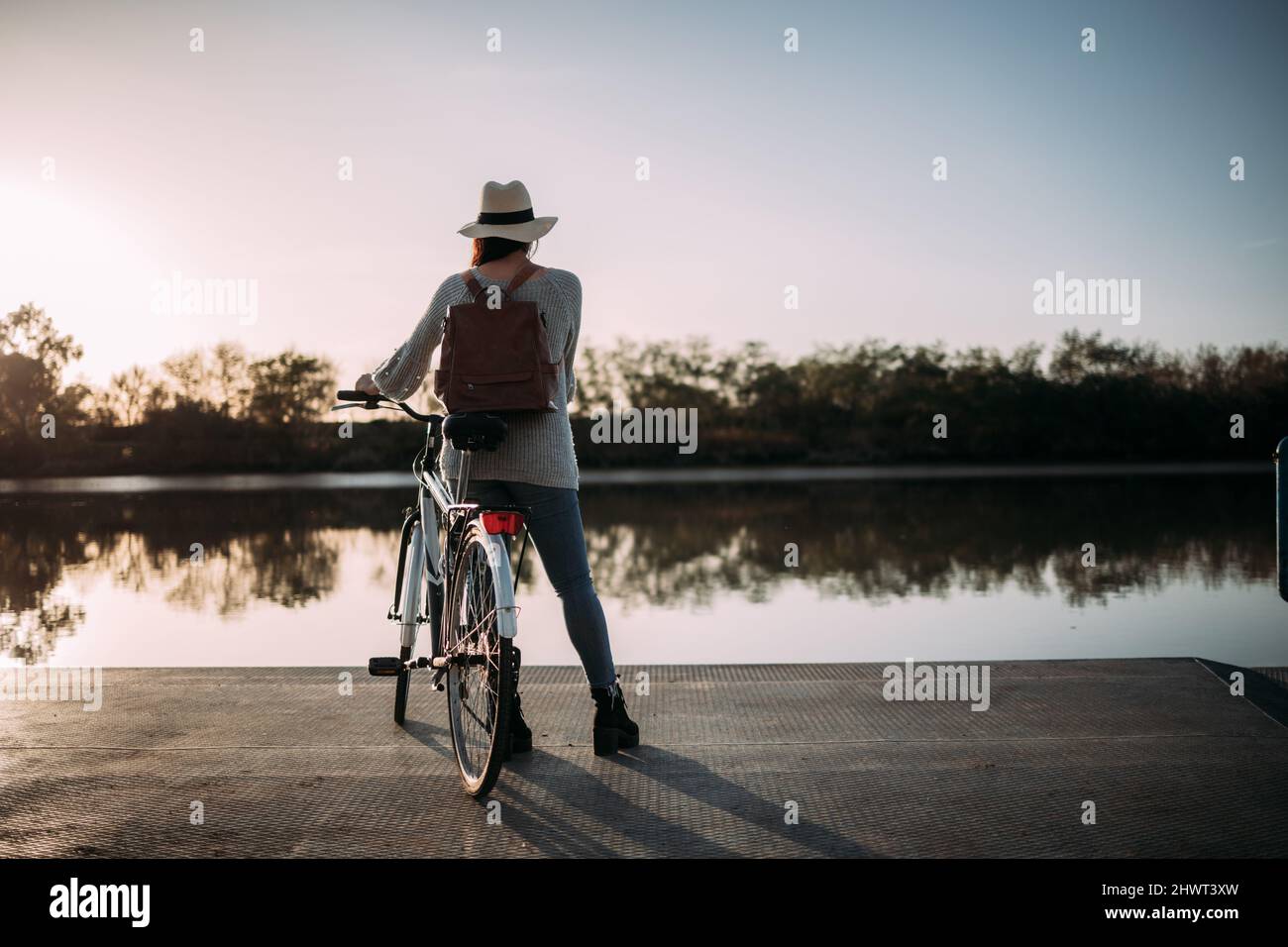 Jeune femme avec chapeau randonnée avec son vélo à un lac Banque D'Images