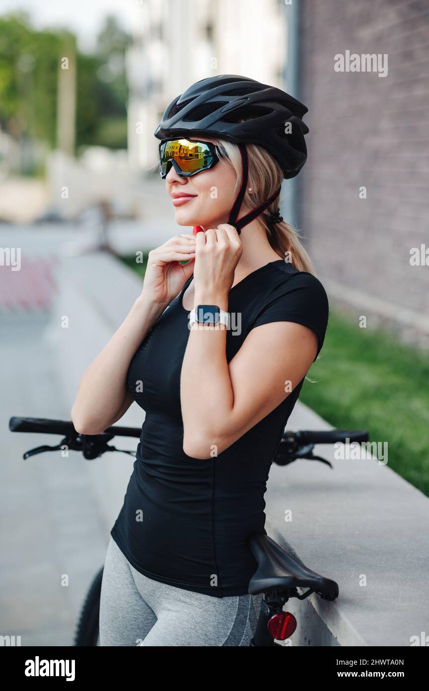 Vue latérale d'une jolie jeune femme portant un casque de sécurité et des  lunettes à miroir, debout dans la rue avec un vélo noir.Cycliste femelle se  préparant pour outd Photo Stock -