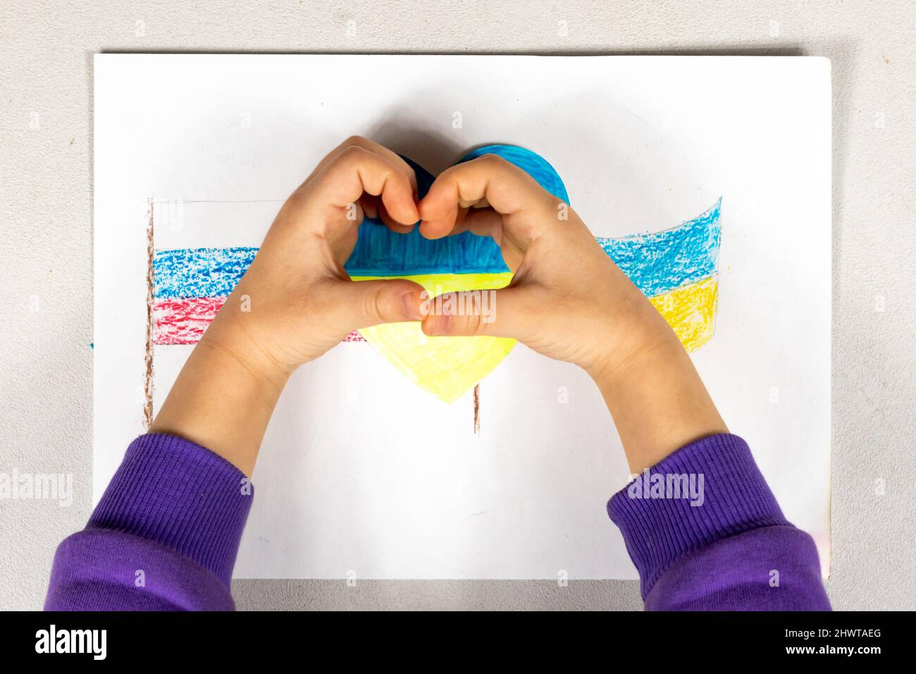 Un enfant fait un signe de coeur avec ses mains sur un dessin de deux drapeaux de l'Ukraine et de la Russie gros plan. Vue de dessus. Les enfants contre la guerre. Banque D'Images