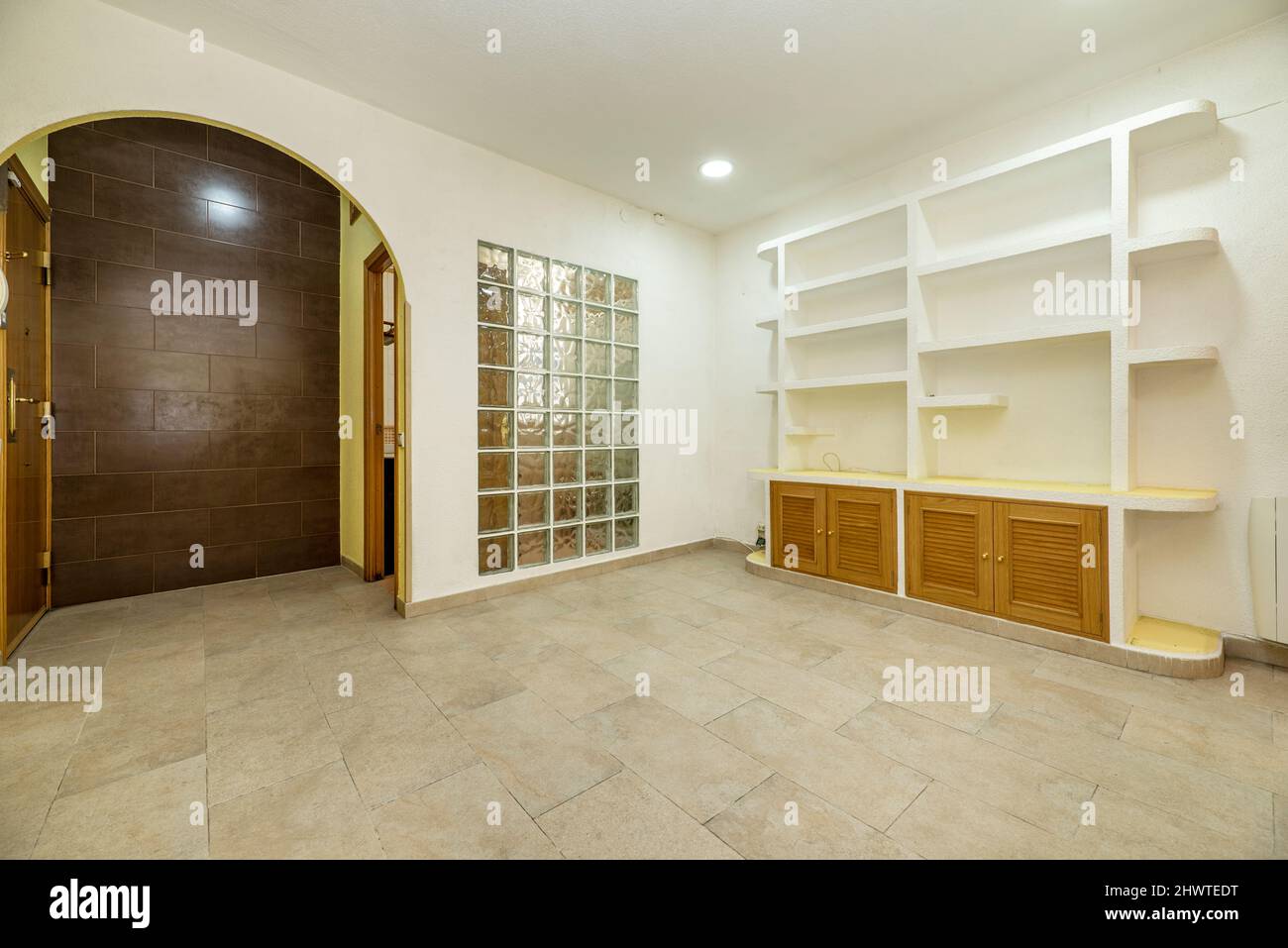 Salon vide avec bibliothèque en plâtre et meubles en bois bas et un mur de  poufs en verre à côté d'une arche semi-circulaire Photo Stock - Alamy