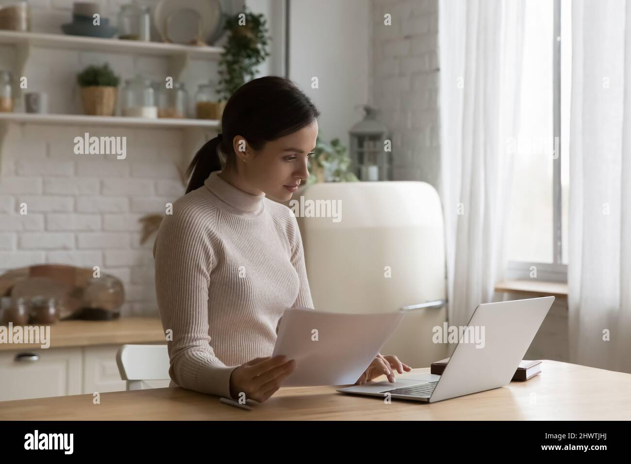 Femme tenant des papiers travaillant à la maison ordinateur portable Banque D'Images