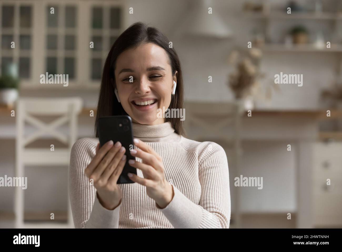 Femme dans des écouteurs sans fil regardant le téléphone portable profiter de la réunion virtuelle Banque D'Images