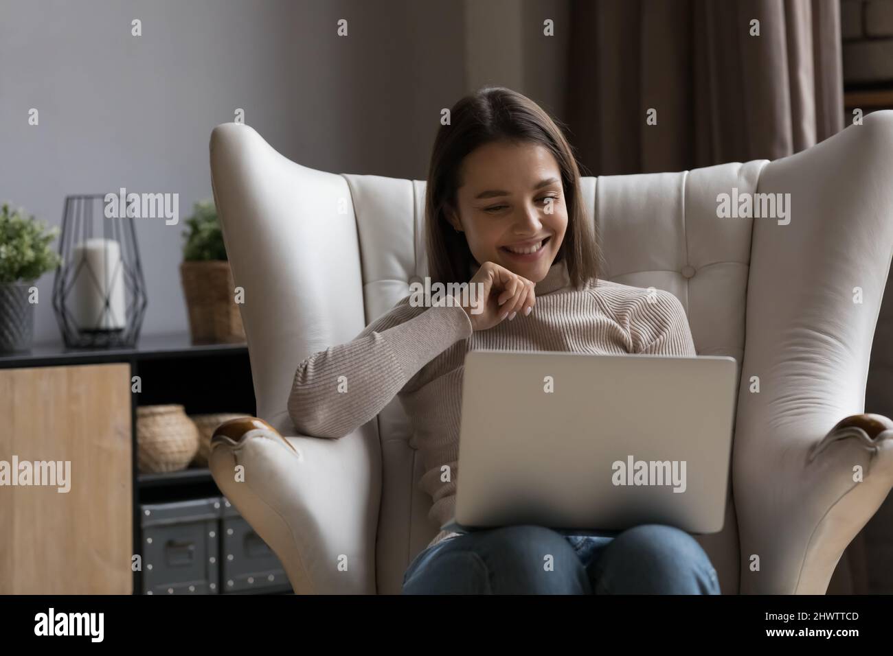 Une femme heureuse s'assoit dans un fauteuil confortable en regardant un ordinateur portable Banque D'Images