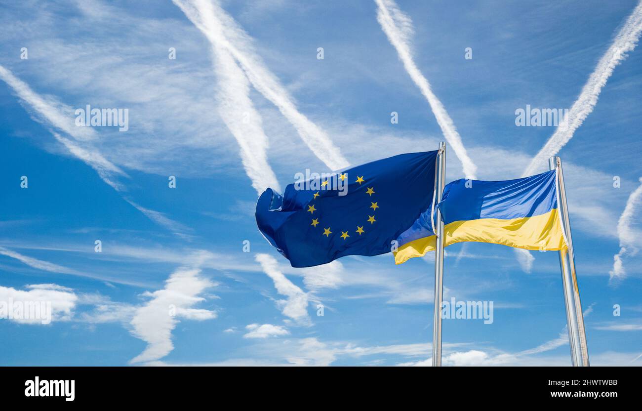 Drapeaux de l'Ukraine et de l'UE, de l'Union européenne contre le ciel bleu avec les avions contrails. Image du concept: Pas de zone de vol, Russie Ukraine conflit, guerre, Europe... Banque D'Images