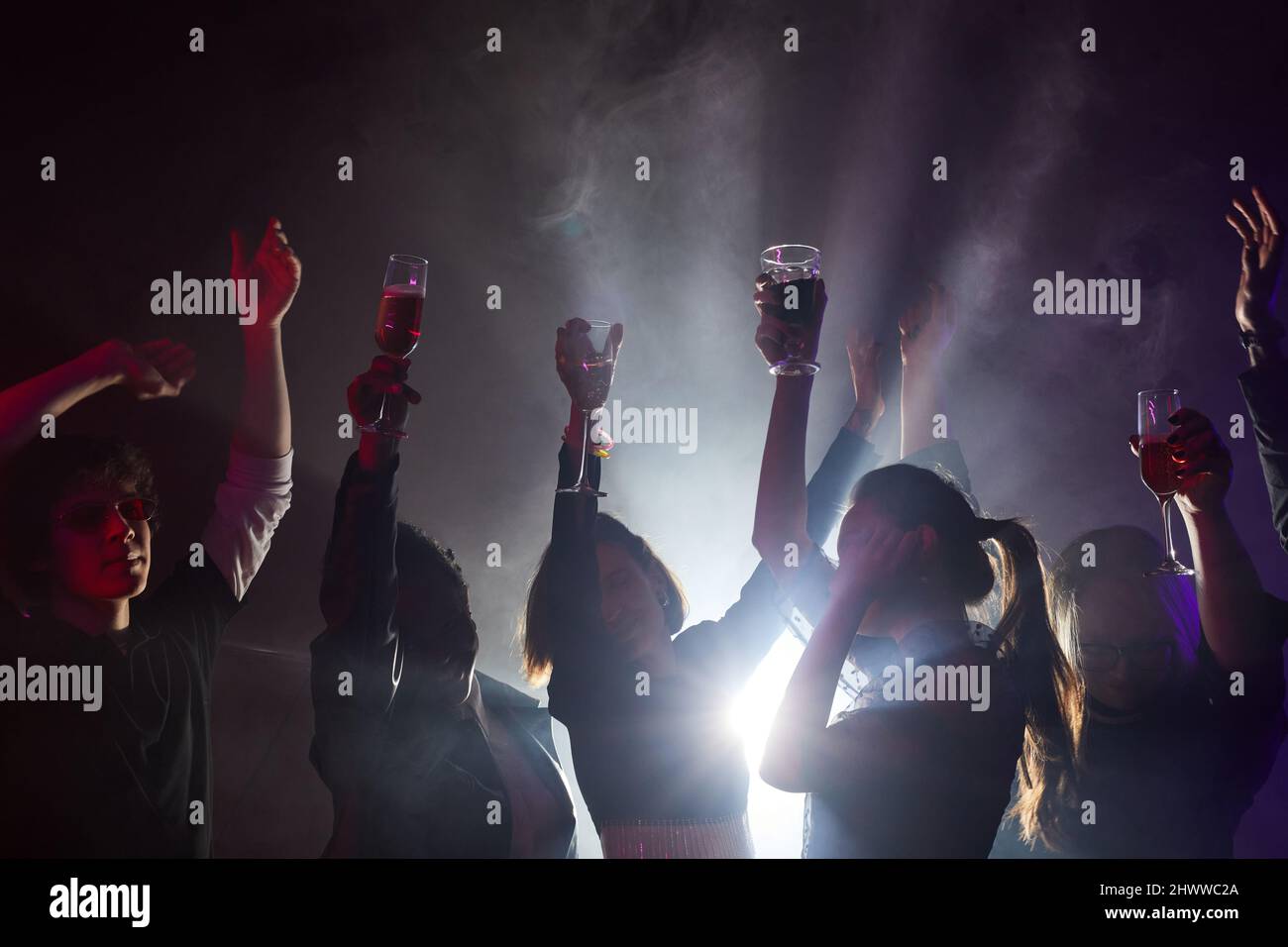 Photo rétro-éclairée de divers jeunes dansant à la fête, silhouettes dans un club enfumé Banque D'Images