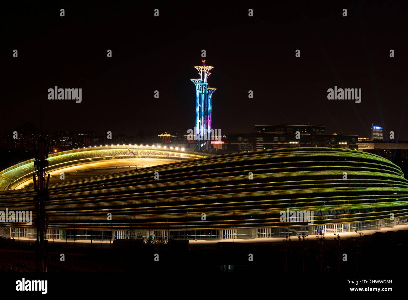 BEIJING, CHINE - 7 MARS 2022 - le Centre national de patinage de vitesse (ruban de glace) brille avec la Tour olympique lors d'un spectacle de lumière la nuit à Beijing, Banque D'Images