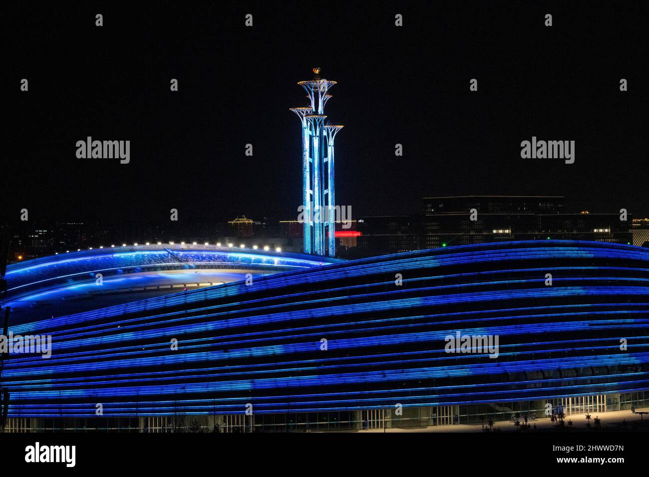 BEIJING, CHINE - 7 MARS 2022 - le Centre national de patinage de vitesse (ruban de glace) brille avec la Tour olympique lors d'un spectacle de lumière la nuit à Beijing, Banque D'Images