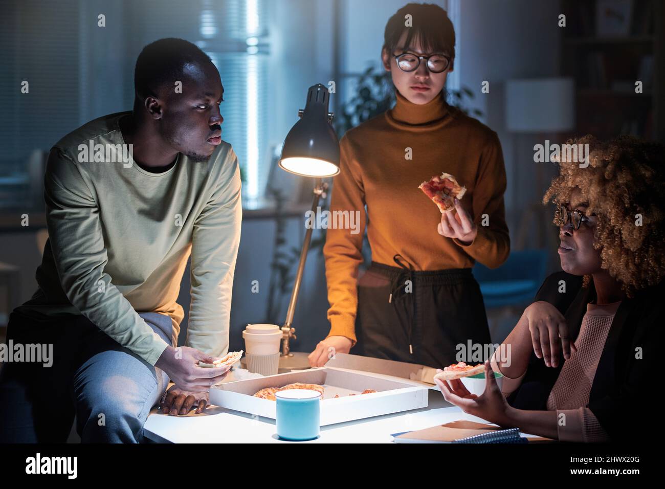 Groupe de gens d'affaires mangeant de la pizza ensemble à la table pendant leur travail d'équipe au bureau jusqu'à tard dans la nuit Banque D'Images