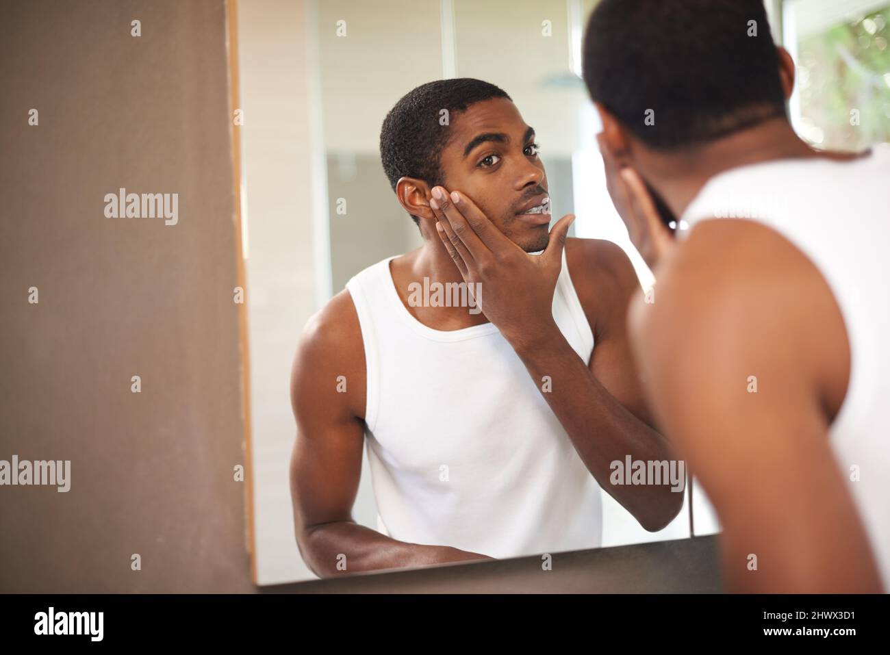 Il prend soin de sa peau. Un jeune homme appliquant de la crème sur son visage tout en regardant dans le miroir. Banque D'Images