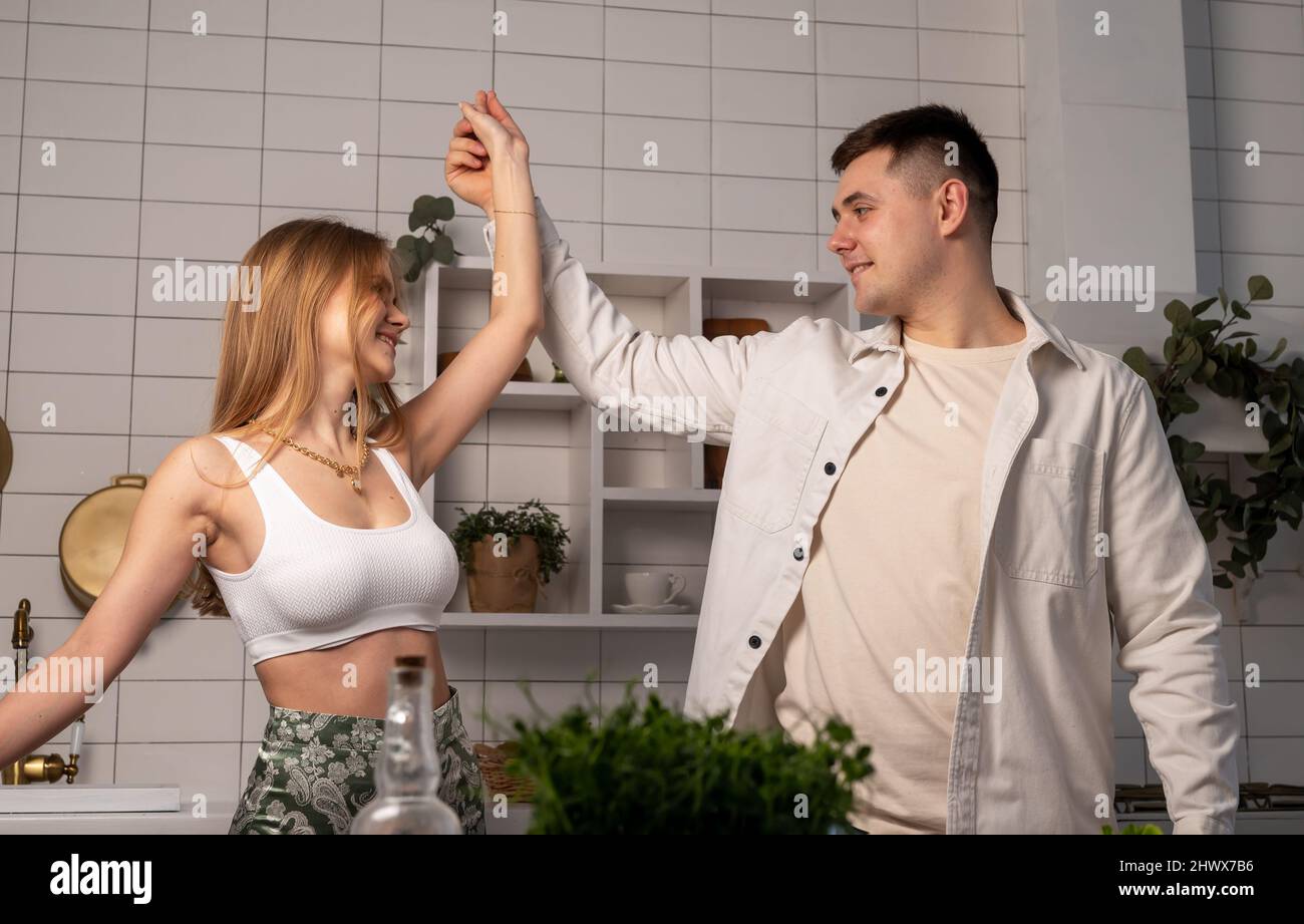 Joyeux jeune couple dansant dans la cuisine moderne tout en cuisinant. Femme et mari souriants s'amusant et se déplaçant à la musique à la maison. Photo de haute qualité Banque D'Images