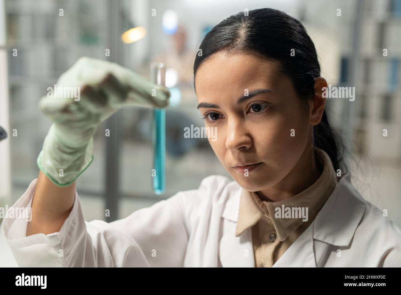 Scientifique contemporain regardant un flacon avec une substance liquide bleue lors d'une expérience scientifique en laboratoire chimique Banque D'Images