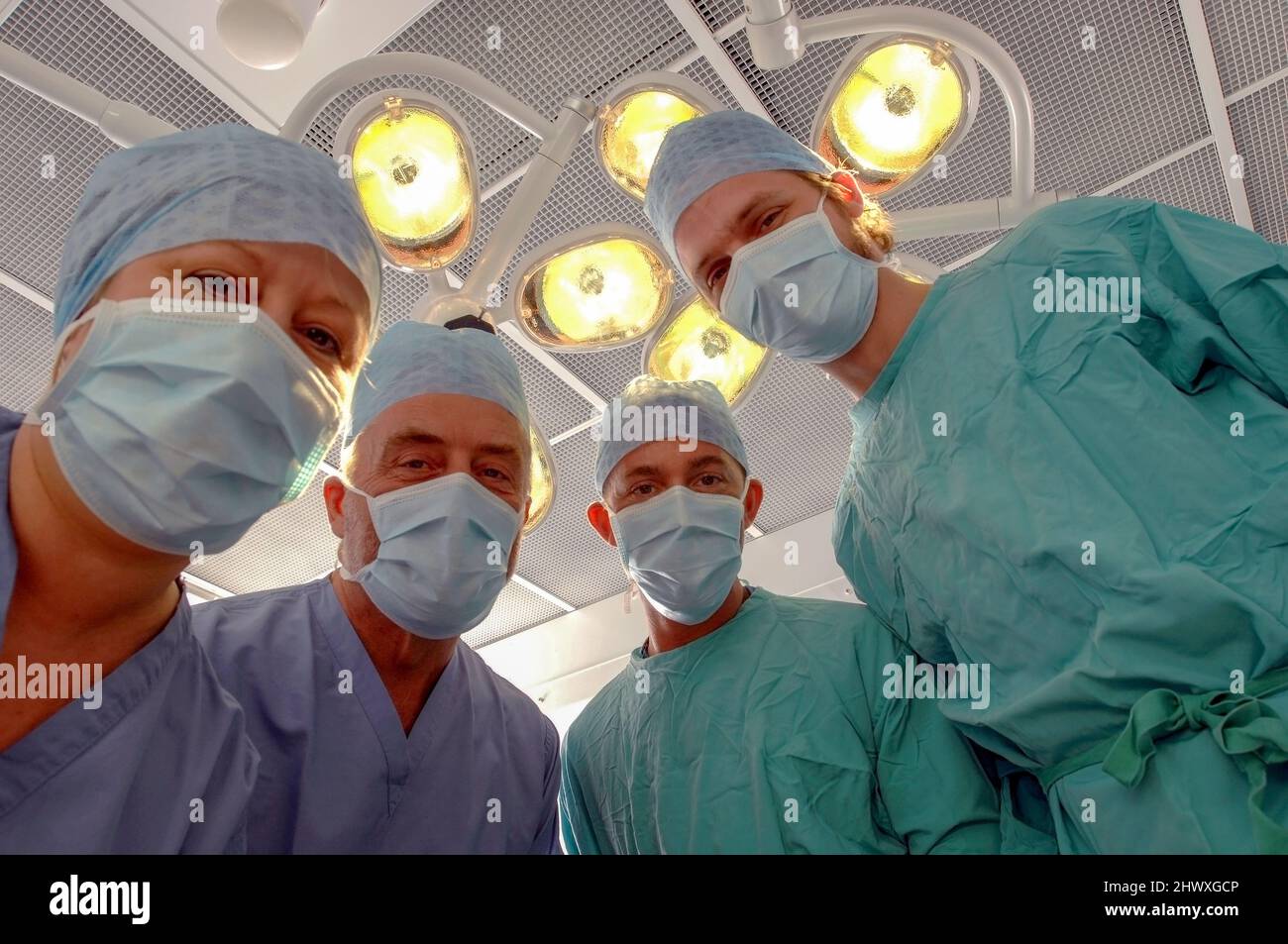 Le point de vue du patient d'une équipe de chirurgiens masqués sous la lumière dans un bloc opératoire de l'hôpital (MODÈLE RELÂCHÉ). Banque D'Images