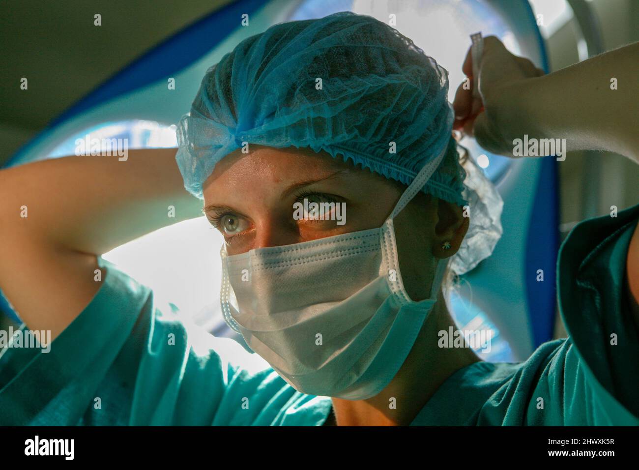 Une femme chirurgien attache son masque chirurgical autour de son visage sous les lumières du théâtre (MODÈLE RELÂCHÉ) Banque D'Images