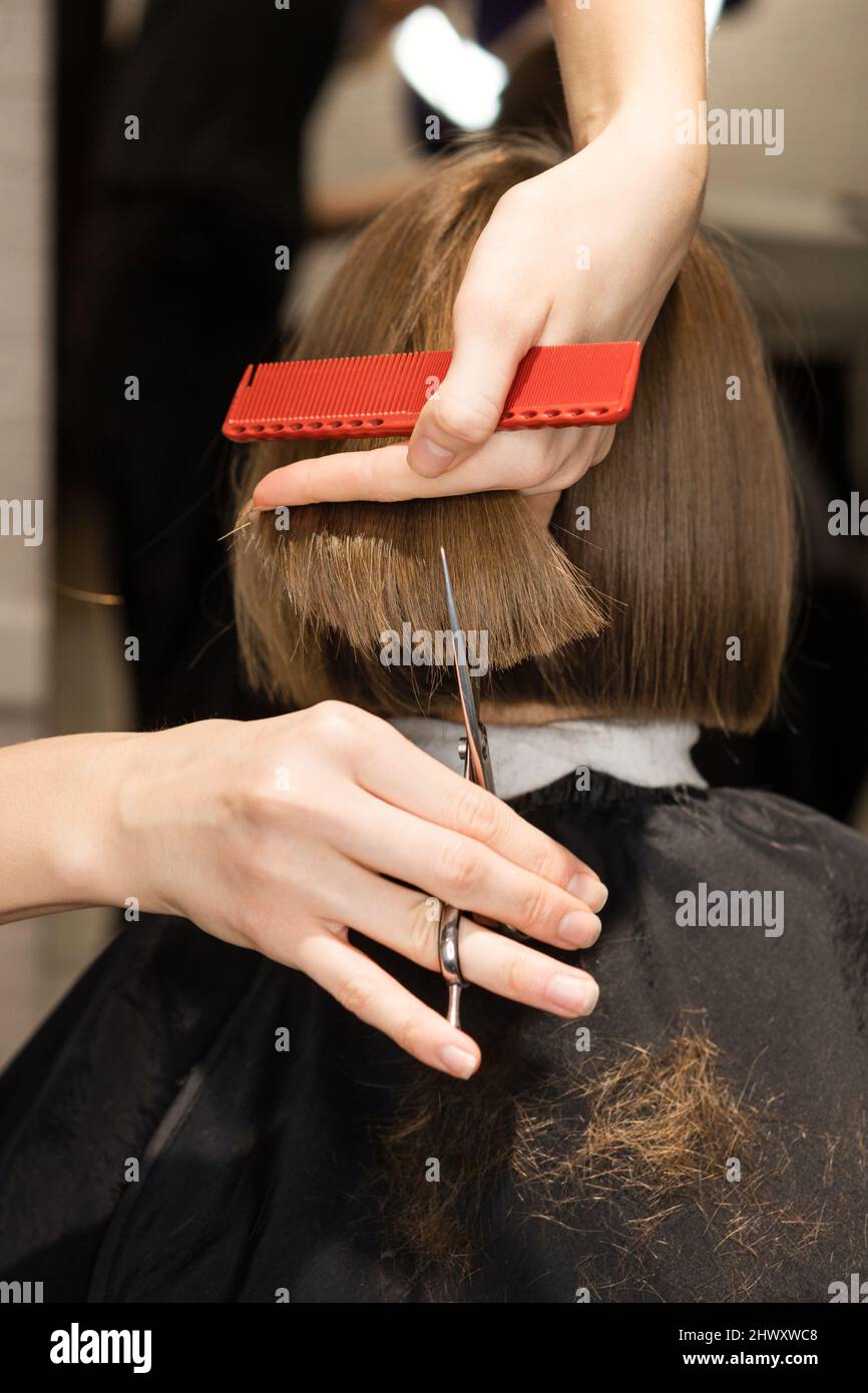 Gros plan arrière de la préadolescence fille assise dans la chaise dans le salon de coiffure. Coiffeur vérifiant sa nouvelle coupe de cheveux Banque D'Images