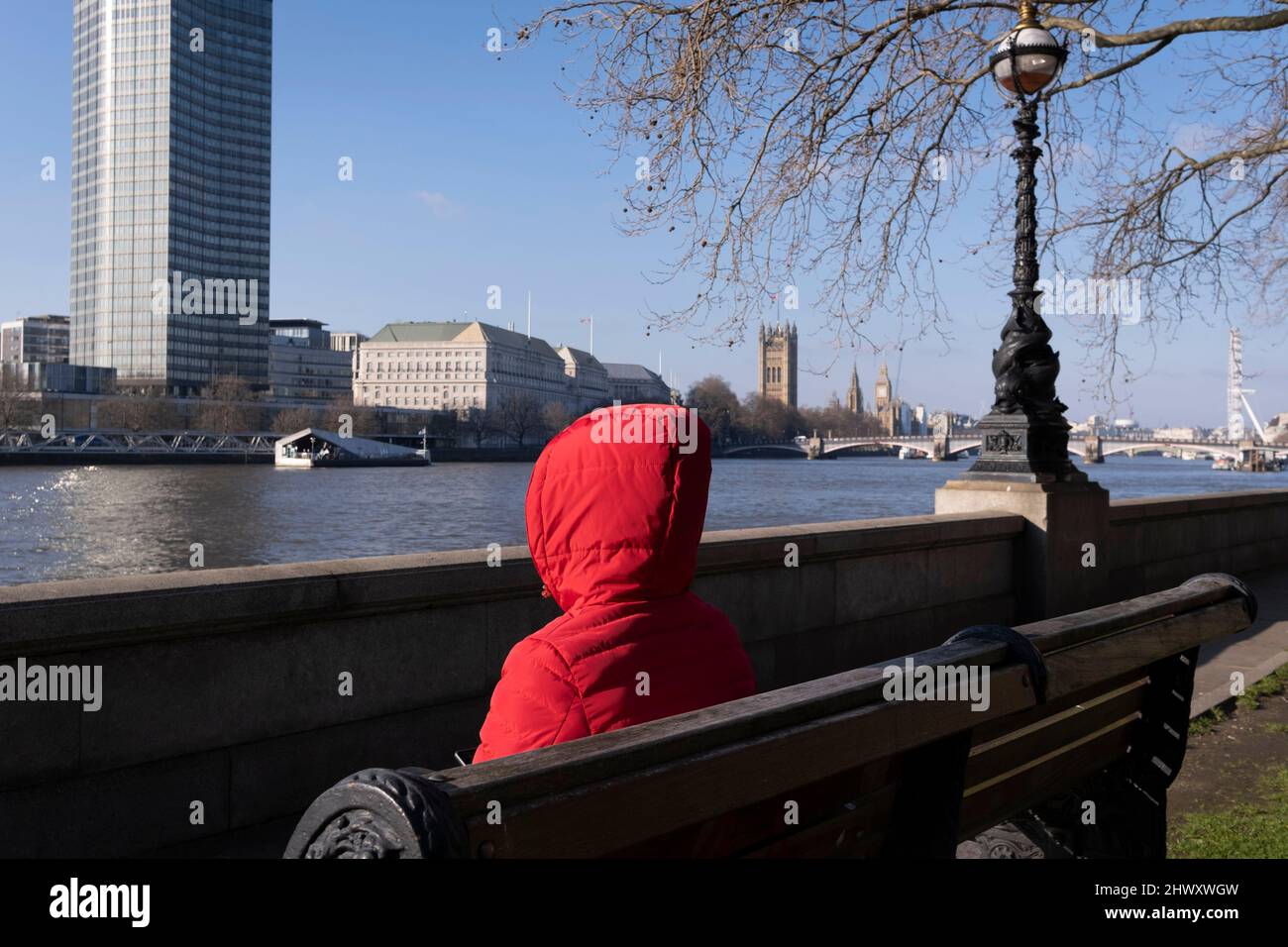 Une personne portant un sweat à capuche rouge s'assoit sur un banc au bord de la rivière qui domine la Tamise où MI5 le service de renseignements du Royaume-Uni est situé, le 7th mars 2022, à Londres, en Angleterre. Banque D'Images