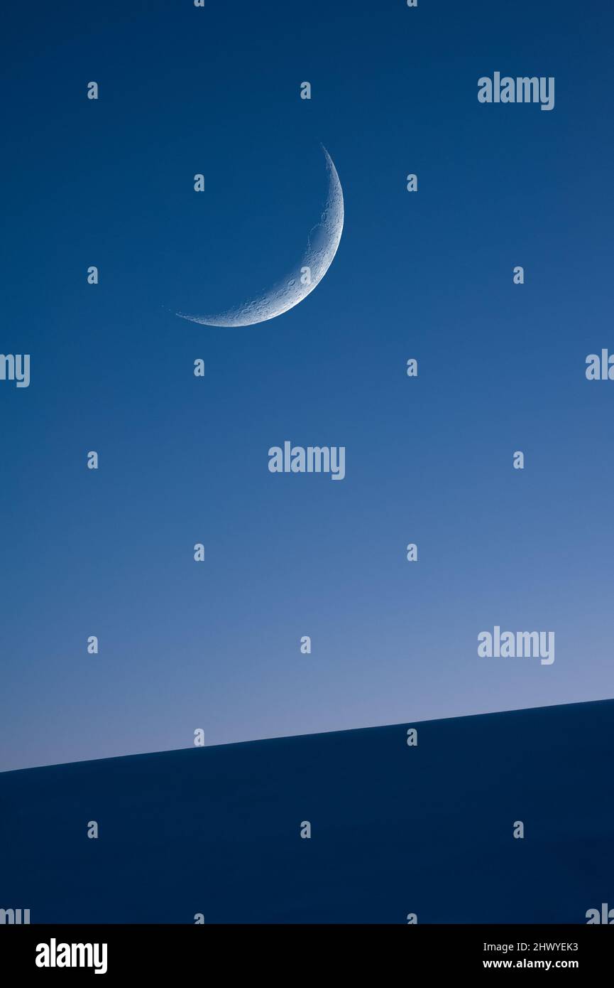 Croissant de cire Lune sur ciel bleu crépuscule. Bord de pente enneigé au premier plan. Banque D'Images