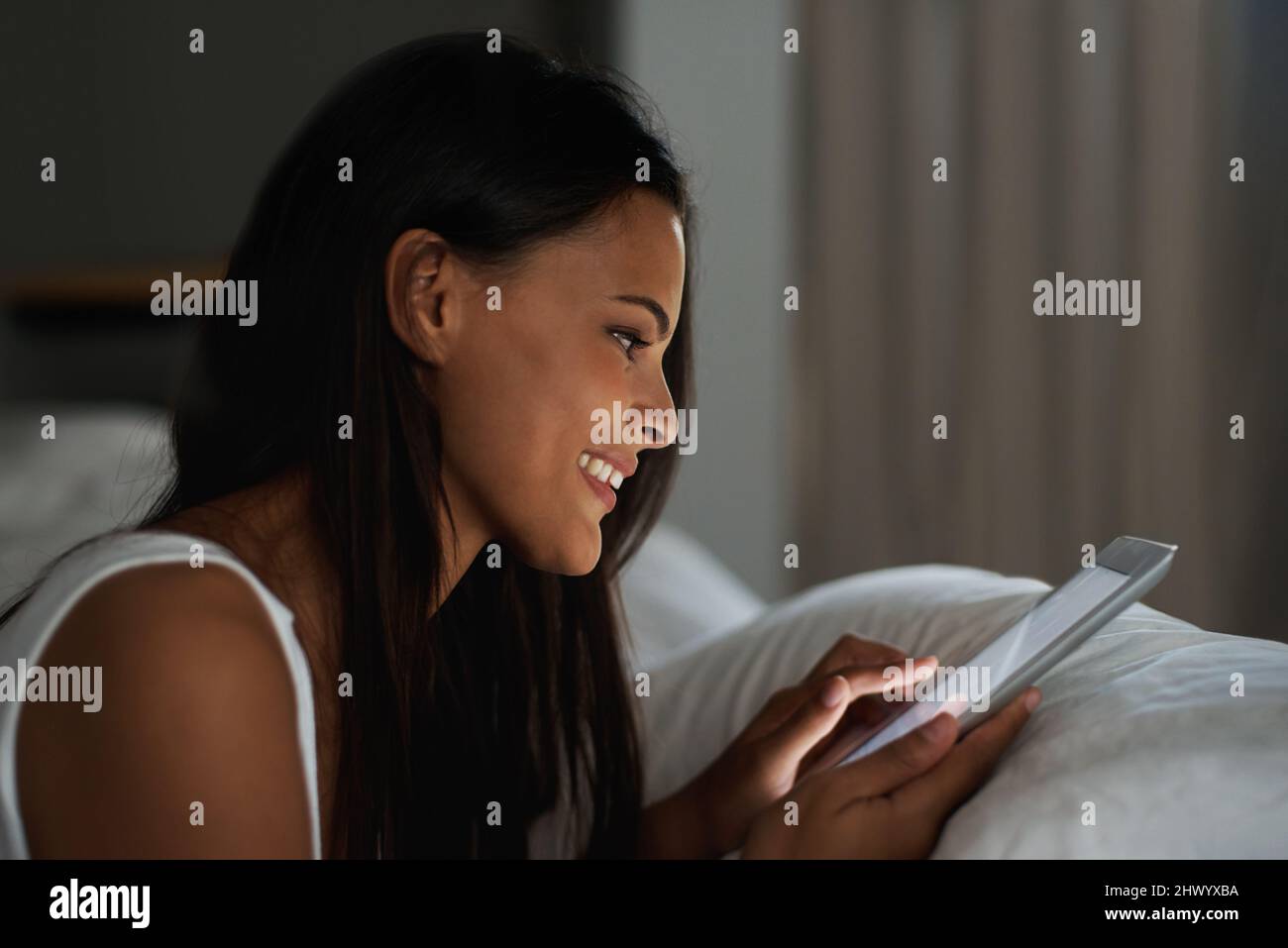 Garder le contact n'a jamais été aussi simple. Photo d'une belle jeune femme se reposant au lit avec sa tablette. Banque D'Images