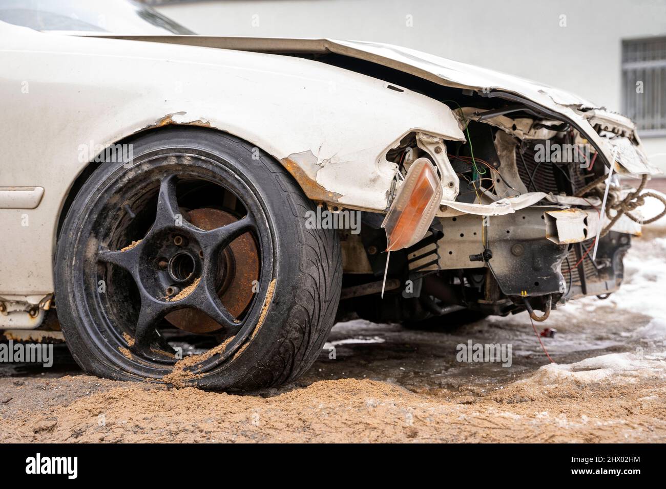 Berline blanche écrasée avec roues noires avec phares, capot et pare-chocs endommagés, voiture jdm japonaise après un accident, vue latérale Banque D'Images