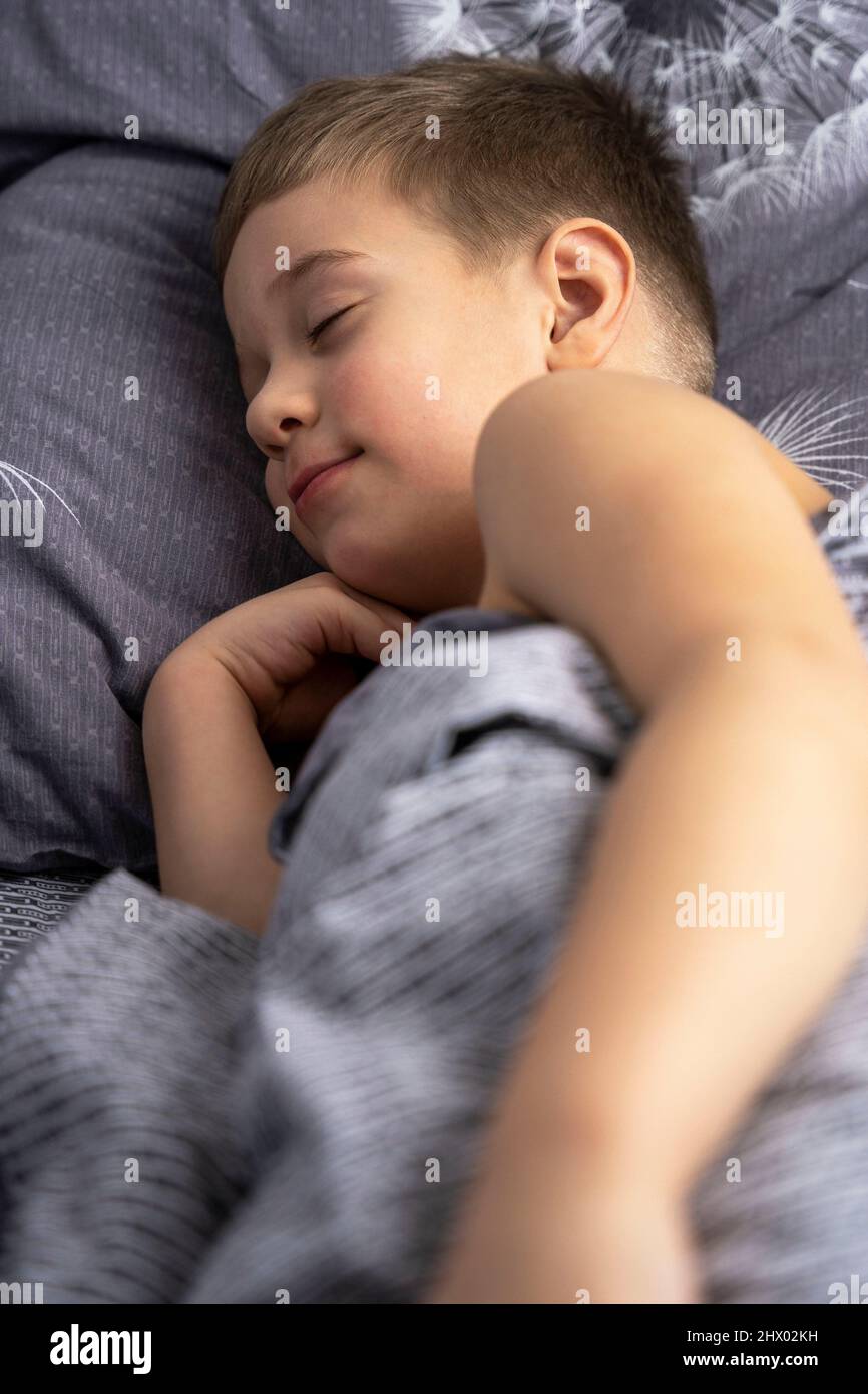 Un mignon petit garçon caucasien de 5 ans dorme dans le lit. Repos, confort à la maison et tranquillité. Banque D'Images