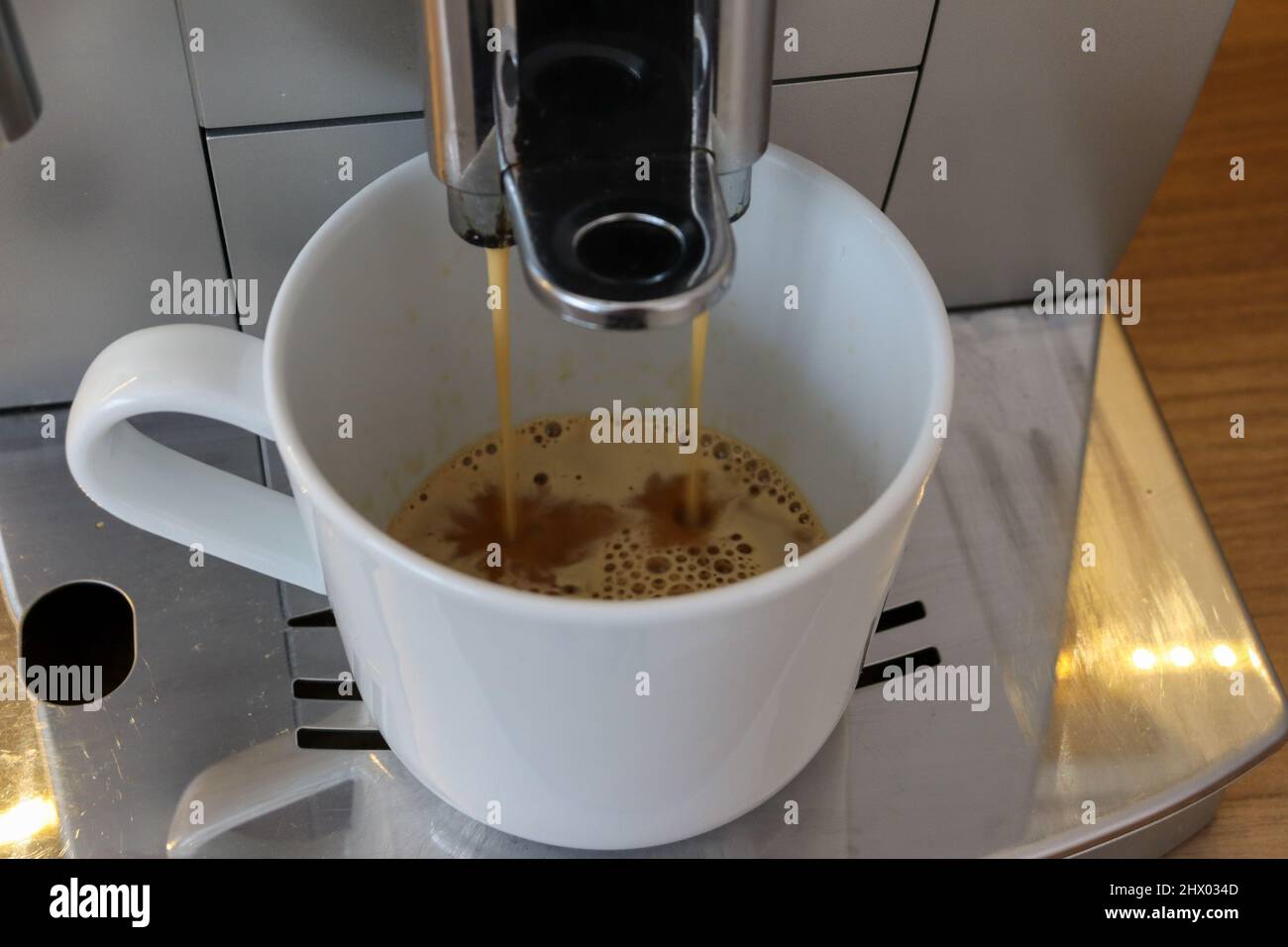 Machine à café à moulin intégré, versez du café frais dans une tasse blanche avec de la crème Banque D'Images