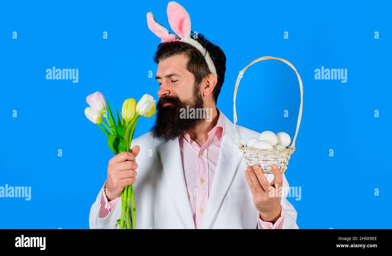 Joyeuses Pâques. Homme barbu avec des oreilles de lapin avec des oeufs de panier et un bouquet de tulipes. Lapin homme. Banque D'Images