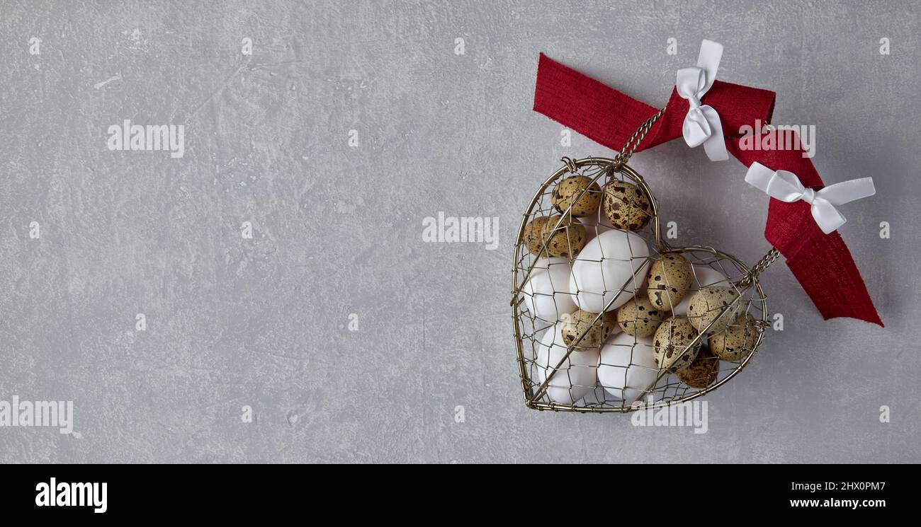 Œufs de poulet et de caille dans un panier métallique tissé en forme de coeur Banque D'Images