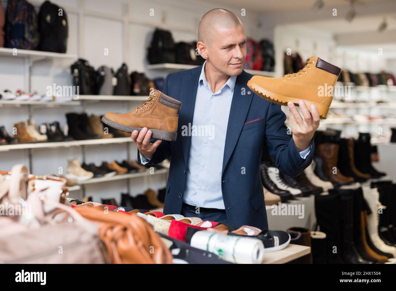 Positif homme choisissant des bottes d'hiver tendance dans le magasin de chaussures Banque D'Images