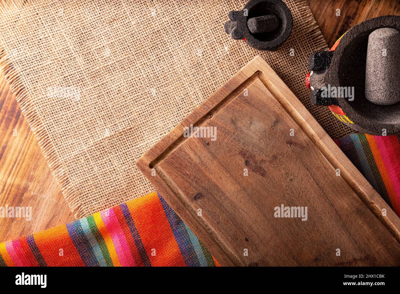 Cuisine mexicaine avec planche à découper vide, tissus traditionnels colorés et molajote sur table rustique en bois. Vue de dessus avec espace de copie. Banque D'Images