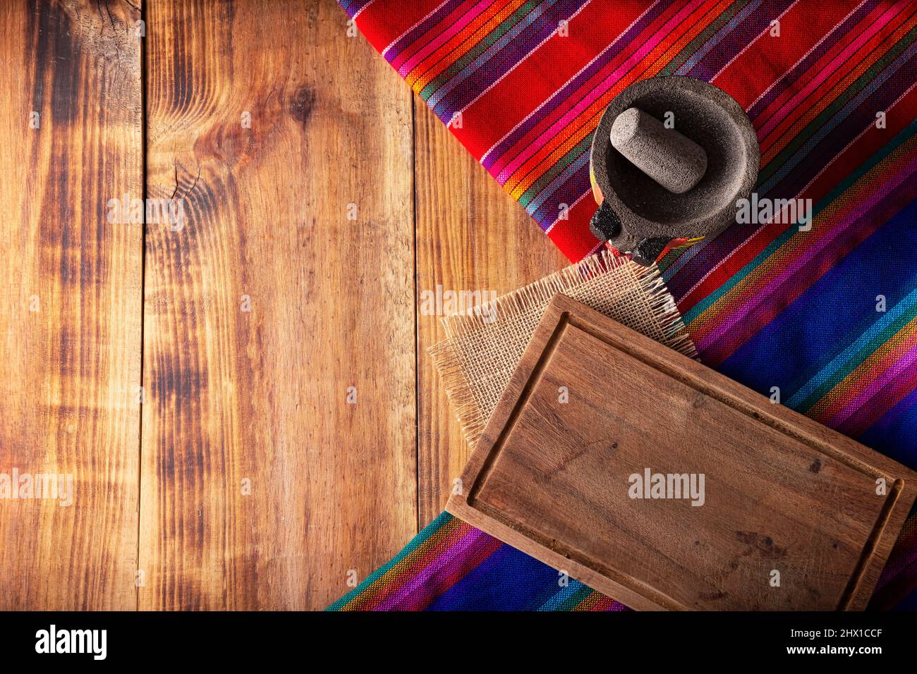 Cuisine mexicaine avec planche à découper vide, tissus traditionnels colorés et molajote sur table rustique en bois. Vue de dessus avec espace de copie. Banque D'Images