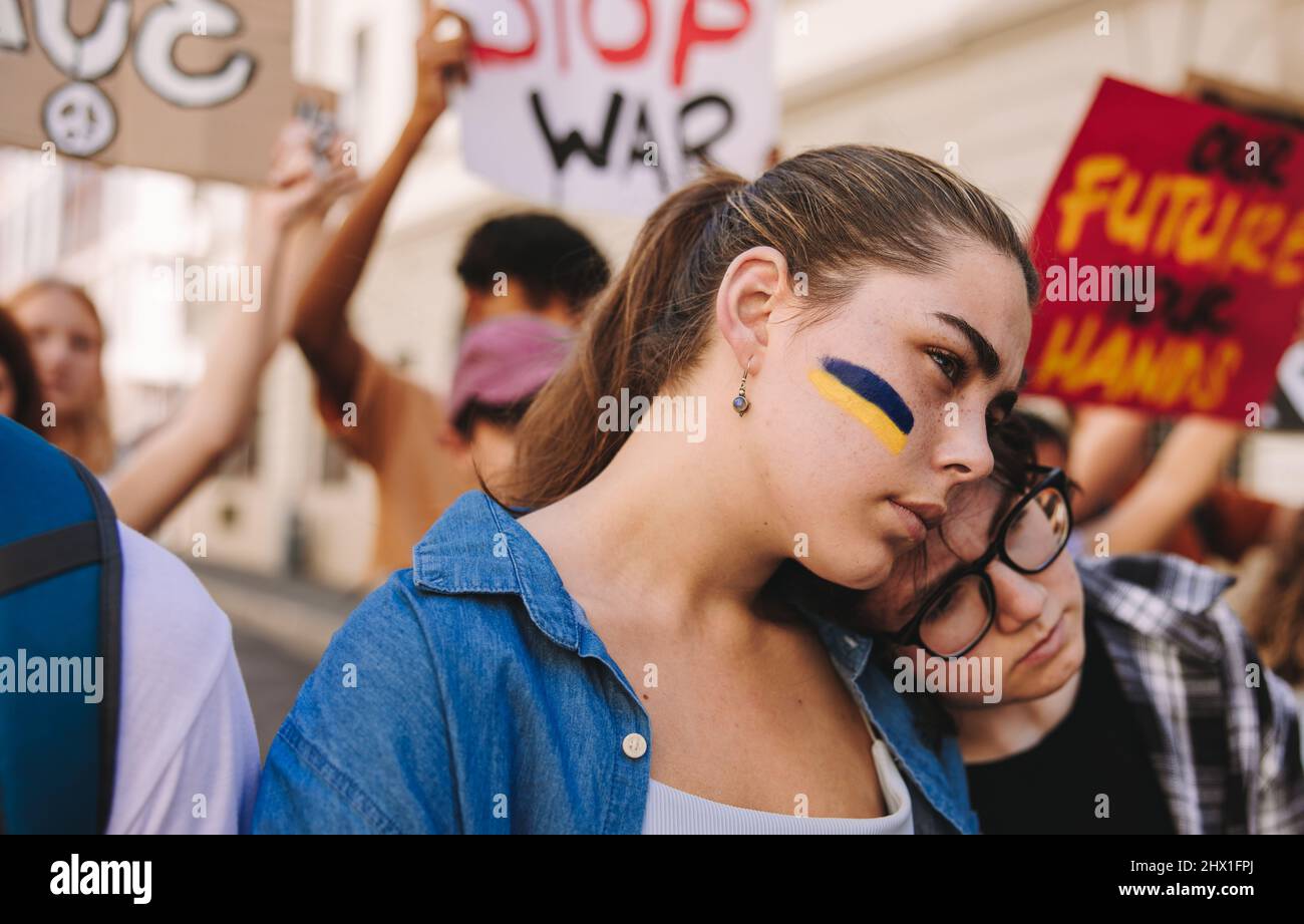 Mettre fin au conflit en Ukraine. Une jeune femme markant contre la guerre avec le drapeau de l'Ukraine peint sur son visage. Groupe de jeunes multiculturels holdin Banque D'Images