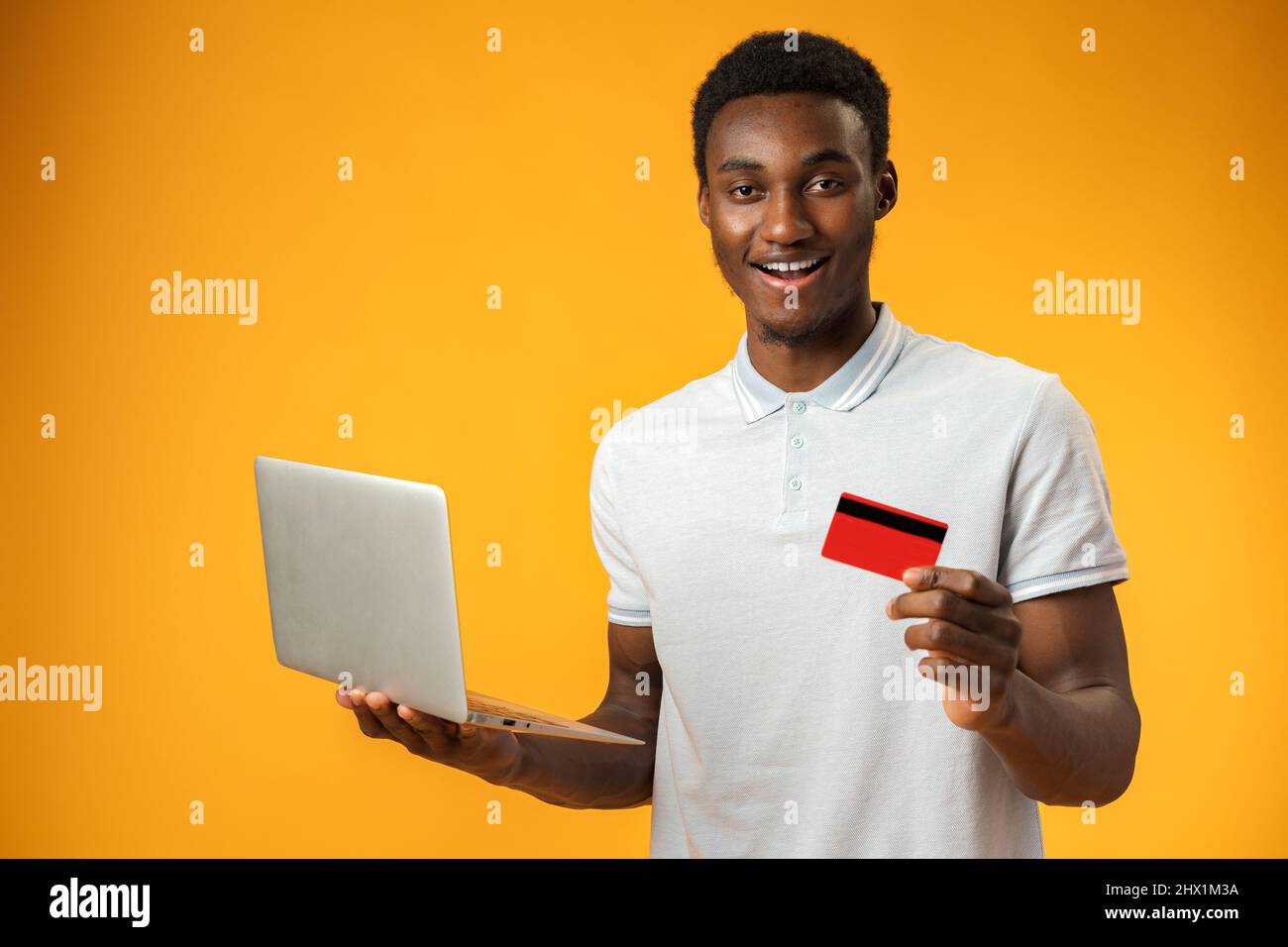 Portrait d'homme noir joyeux avec ordinateur portable et carte de crédit sur jaune Banque D'Images