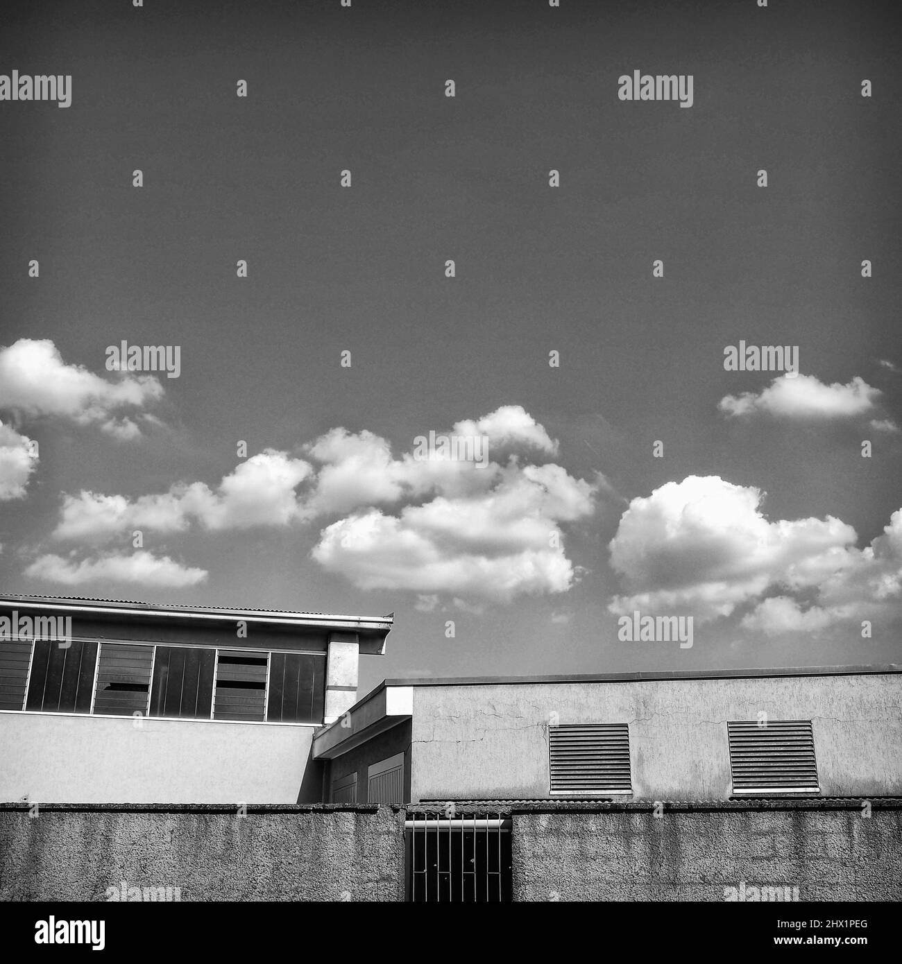 Photographie d'art noir et blanc de hangar industriel avec nuages blancs dans le ciel Banque D'Images