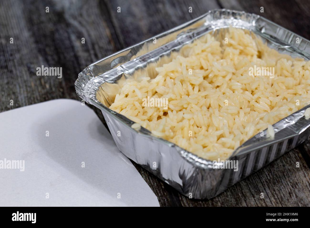 Portion de riz dans un récipient à emporter en papier d'aluminium et couvercle.Sur fond en bois Banque D'Images
