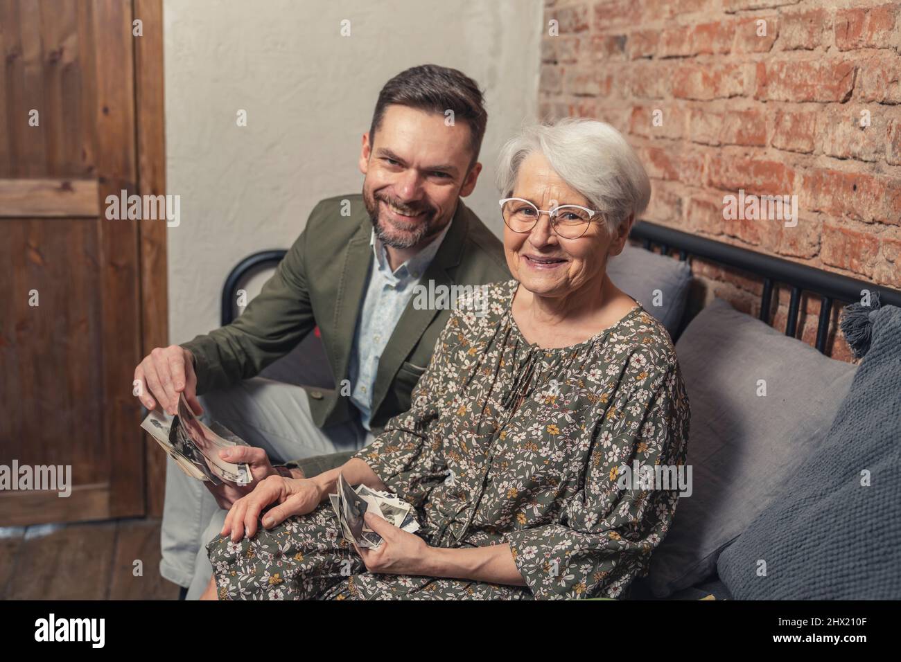 deux membres de la famille assis sur un canapé souriant et regardant l'appareil photo tout en triant les vieilles photos du passé de femme âgée. Photo de haute qualité Banque D'Images