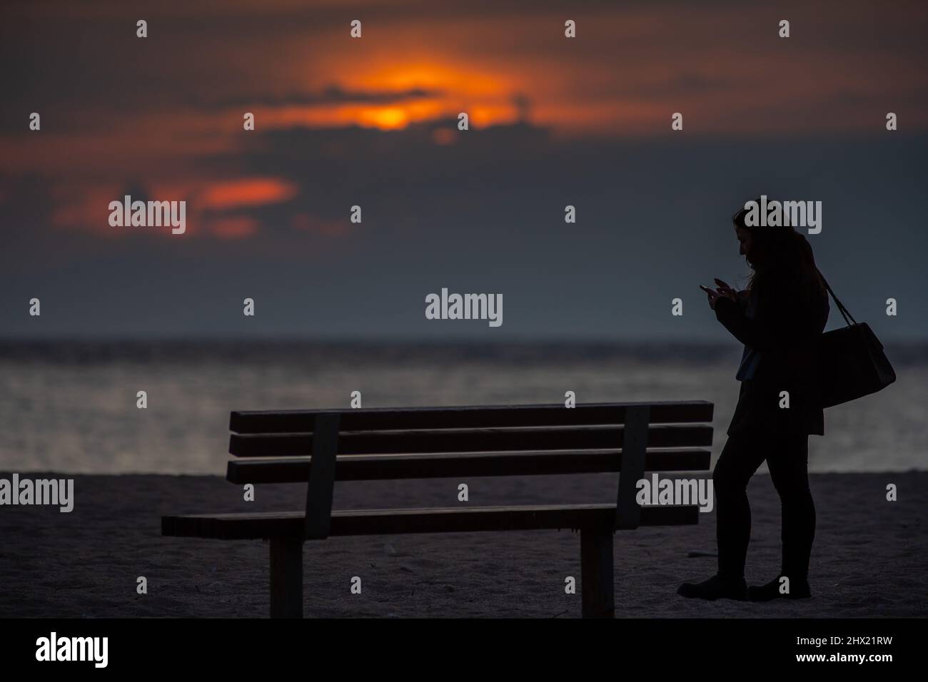 Une dame regardant son téléphone en attendant une plage solitaire Banque D'Images