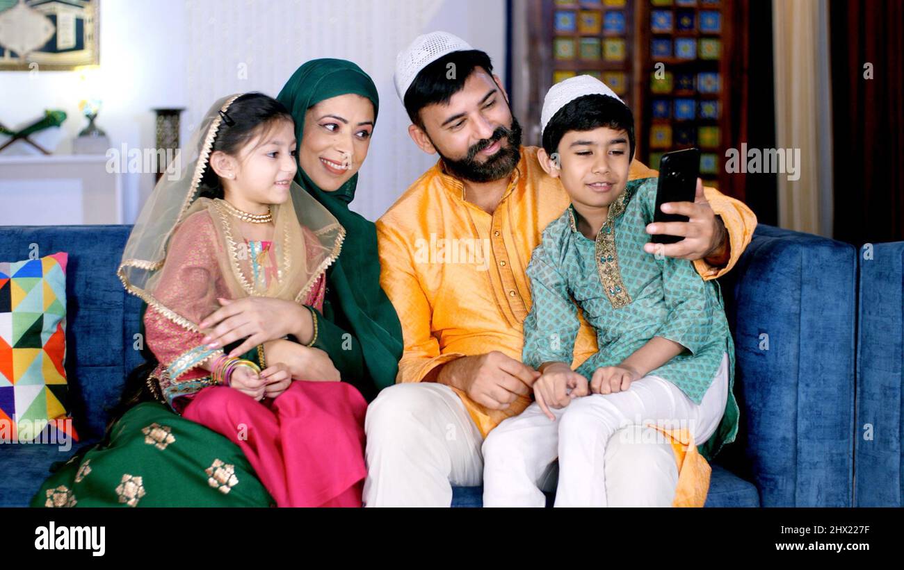 Une famille musulmane joyeuse effectuant un appel vidéo sur son smartphone à la maison. Une famille indienne joyeuse utilisant un mobile ensemble tout en étant assis ensemble Banque D'Images