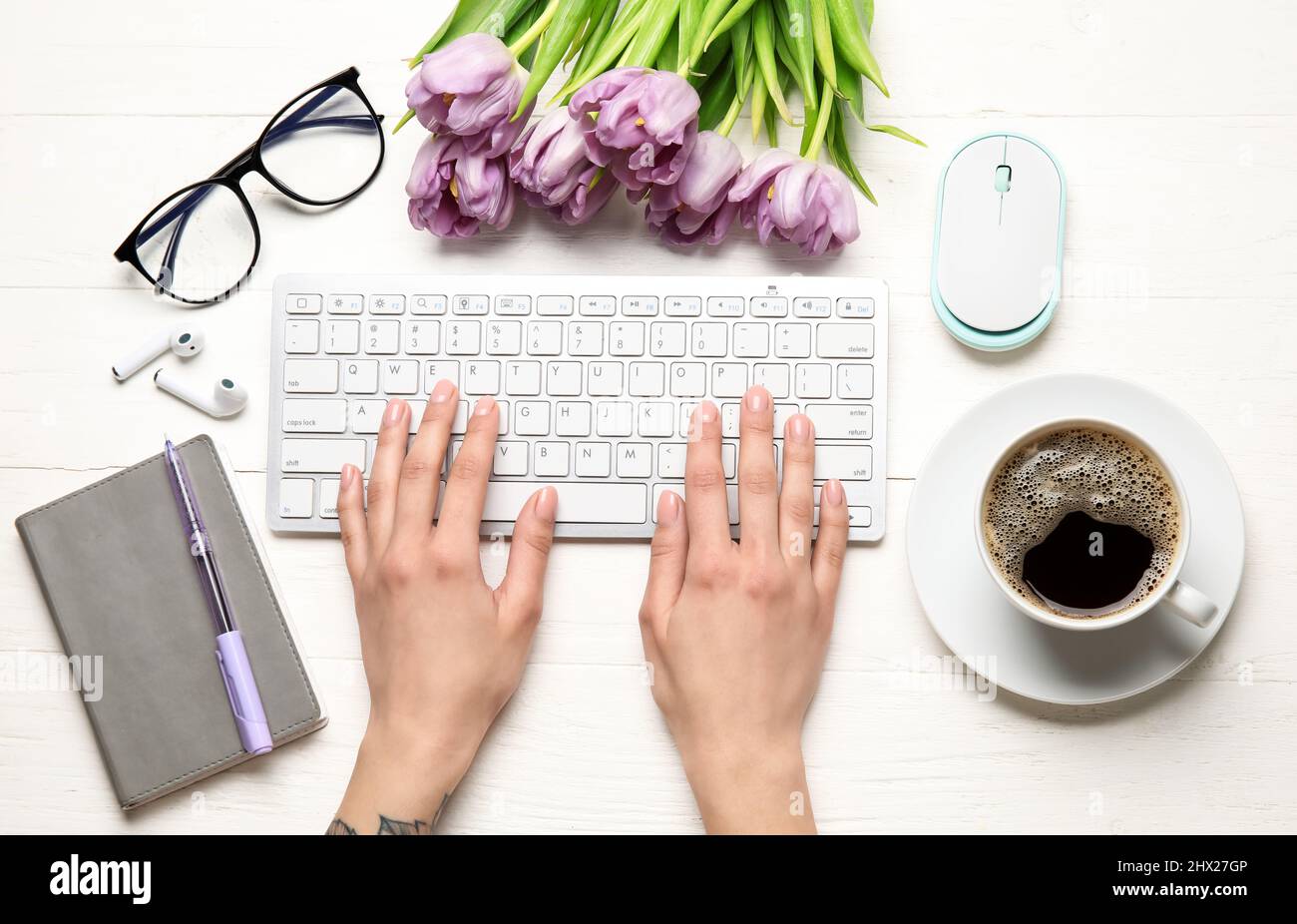 Mains de femmes avec clavier, tasse de café, fleurs de tulipe, écouteurs et lunettes sur fond de bois clair Banque D'Images
