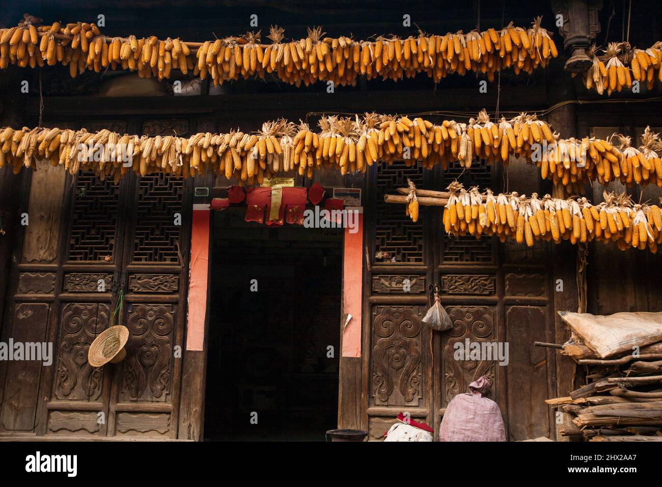 Extérieur d'une ancienne maison chinoise, maïs sec suspendu sur le linteau au-dessus de la porte en bois. Chengzi Village, l'ancien village du Yunnan, en Chine. Banque D'Images