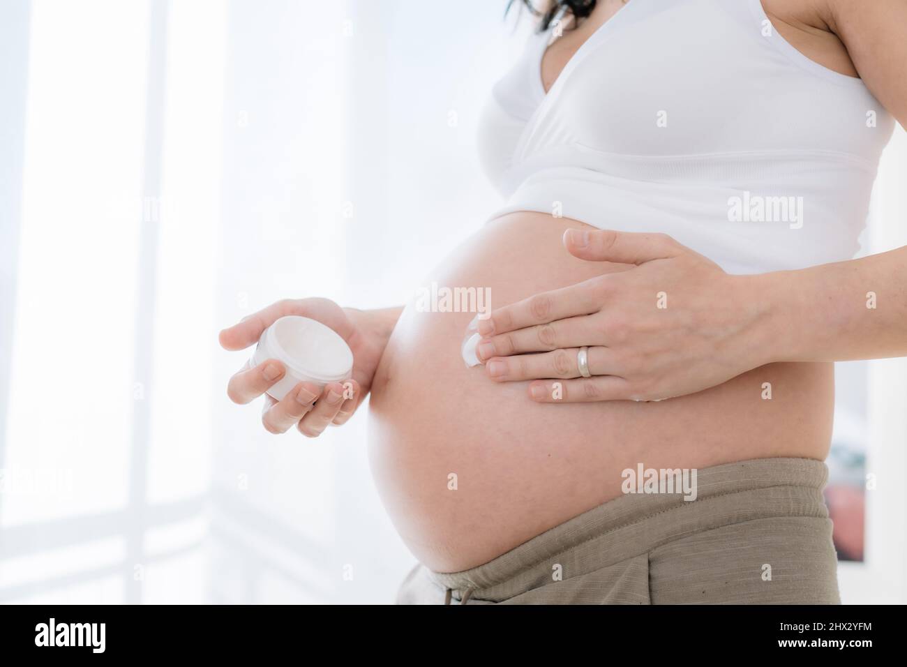 la jeune femme enceinte applique de la crème hydratante sur son ventre pour lisser la peau. Prévention des marques de tension pendant la grossesse. Santé et soins du corps concep Banque D'Images