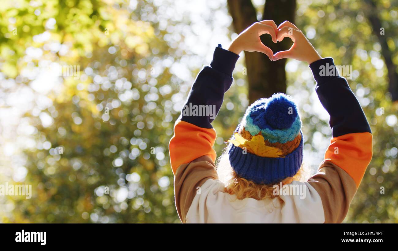 Jeune femme blonde tenant les mains en forme de coeur romantique dans le parc - copie d'espace moyen. Photo de haute qualité Banque D'Images