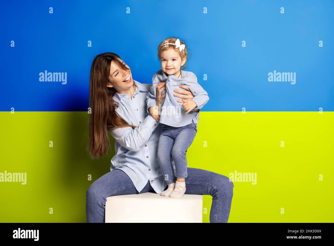 Portrait de la jeune femme, mère avec sa petite fille, fille isolée sur fond bleu et jaune drapeau ukrainien Banque D'Images