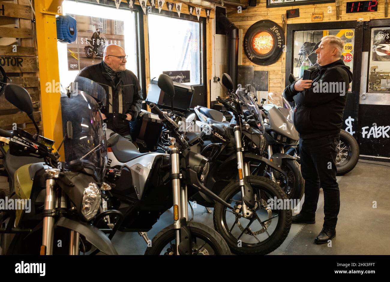 Deux passionnés de moto bavardes dans une salle d'exposition spécialisée dans les motos électriques. Banque D'Images