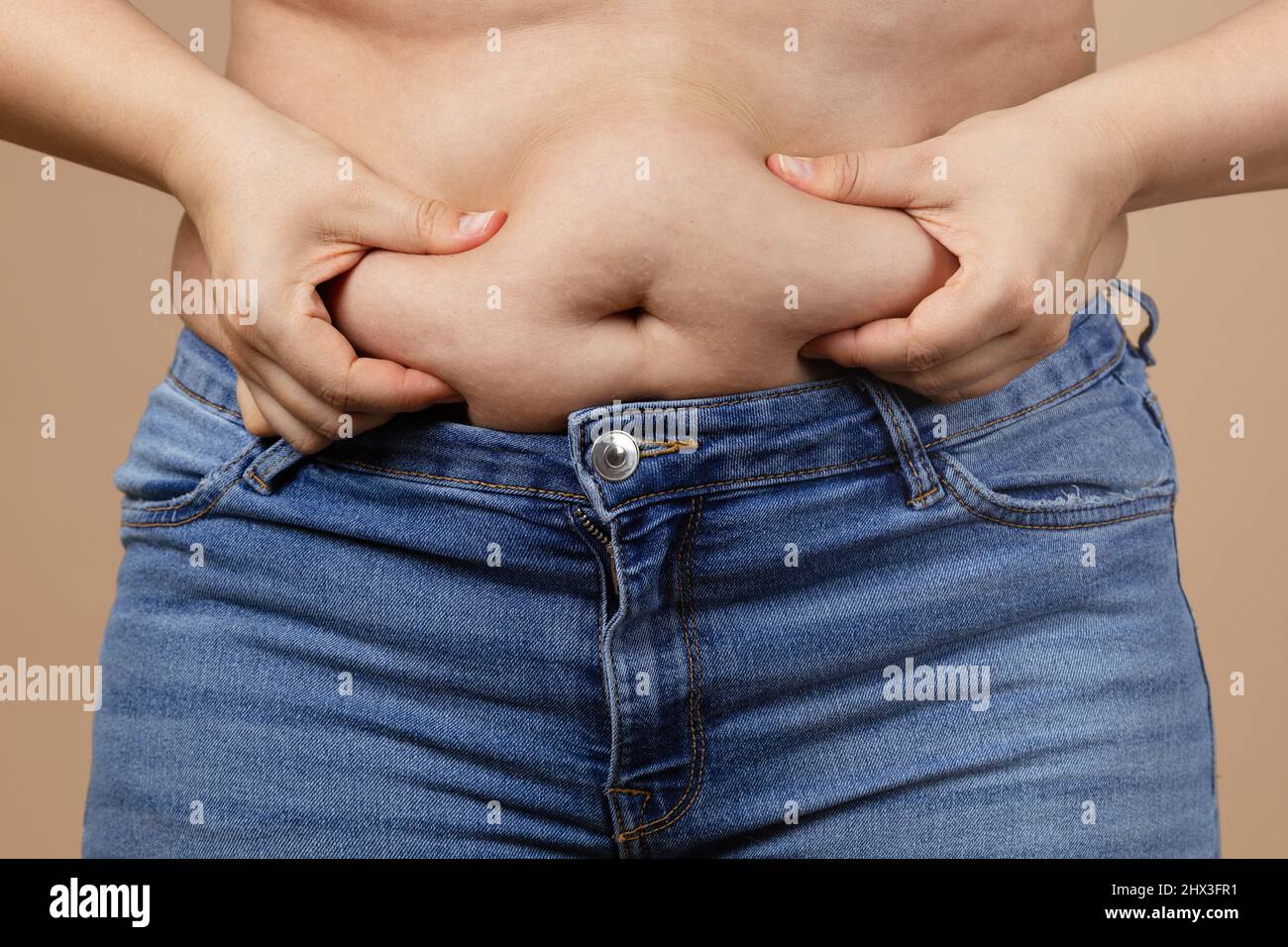 Femme de graisse caucasienne touchant le ventre surpondéré avec les mains portant des jeans bleus. Graisse viscérale. Corps positif et s'acceptant vous-même. Gain de poids soudain Banque D'Images