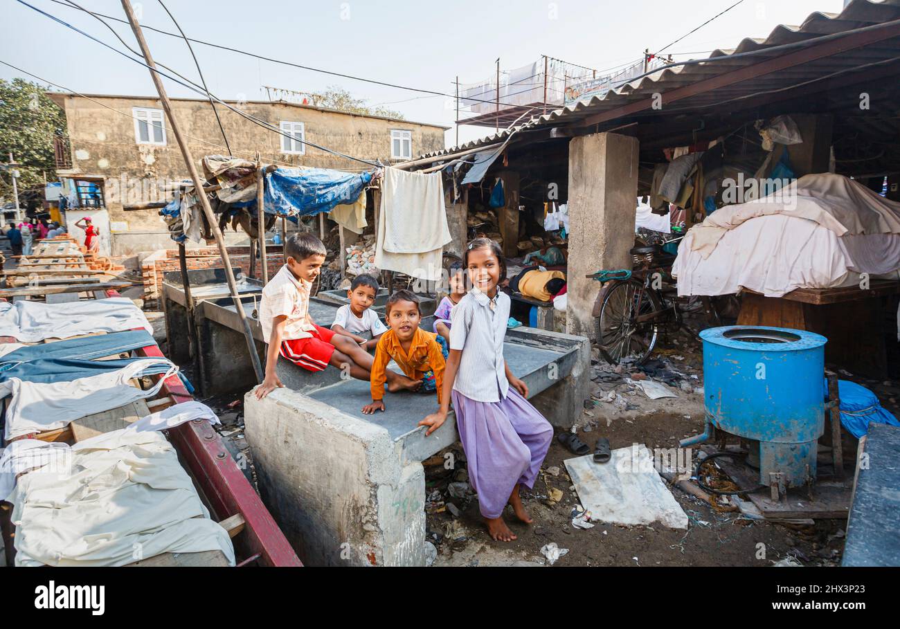 Les enfants, les garçons et les filles de la région, jouent avec joie parmi les vêtements de séchage sur un stylo de lavage à Mahalaxmi Dhobi Ghat, une grande buanderie en plein air à Mumbai, en Inde Banque D'Images