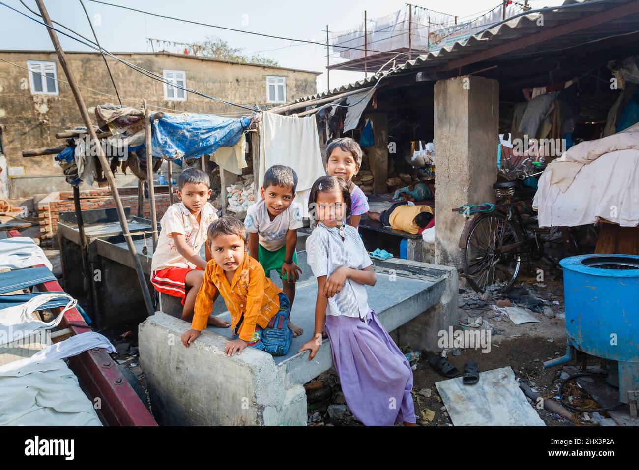 Les enfants, les garçons et les filles de la région, jouent avec joie parmi les vêtements de séchage sur un stylo de lavage à Mahalaxmi Dhobi Ghat, une grande buanderie en plein air à Mumbai, en Inde Banque D'Images